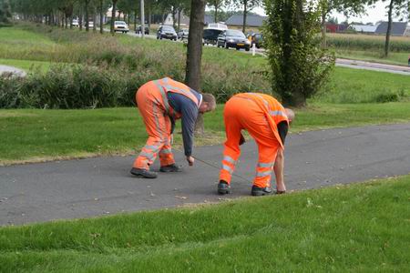 De reflectielijntrekkers aan het werk. Eerst in hoog tempo met behulp van een meetlint op het midden van het fietspad streepjes zetten, tot aan de druk bereden N355.   