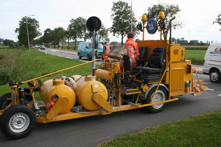 Een collega reflectielinoloog komt met een indrukwekkende machine helderwitte strepen zetten, even de drukte op de N355 trotserend. De machine poept als het ware korte, witte strepen op het wegdek van het fietspad.  