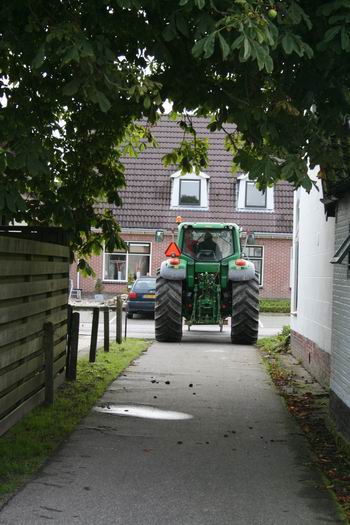 Tractor met dakpannen verlaat het oude Dorpssteeterrein op weg door het dorp naar de Noordwijkweg.