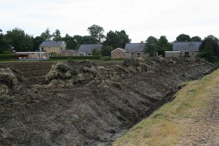 Ingrijpend grondwerk op het land van boer Den Besten. Van twee lappen grond een gemaakt, sloot weggewerkt. Zicht op de achterkant van de woningen aan de Langestraat Noord.  