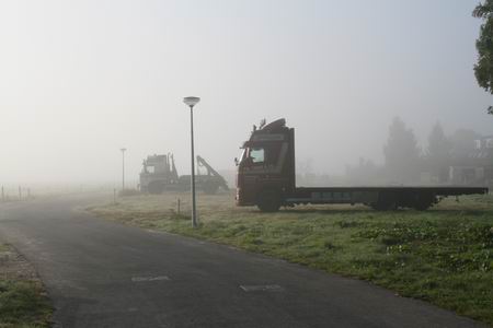 Rechtsaf naar de nieuwe Meidoornstraat waar de silhouetten van twee trucks scherp afsteken tegen de mistige achtergrond.