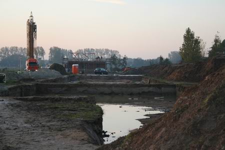 Als ik kom aanlopen, donderdagmorgen, ongeveer half negen, zie ik de verte de hijskraan in ruststand, en het wachtende huis van de familie Kooi. Klaar om de dakdelen te ontvangen. Op de voorgrond de bouwputten van starterswoningen en luxere tweeondereenkappers, nogal waterrijk... 