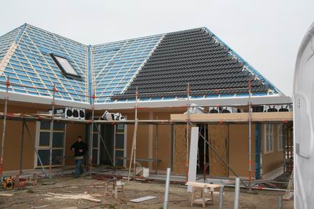 Op het nieuwe huis van Henk Bakker liggen de eerste dakpannen. De VDM-medewerkers timmeren verder dat het een lust is, in het Fries...  