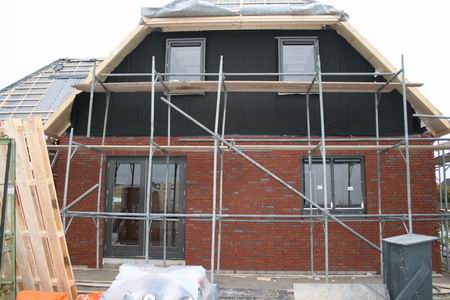 De glaszetter maakt het verblijf in de nieuwe woning van de familie Kooi prettiger. Binnenkort worden de dakpannen gelegd en de muren verder opgemetseld.  