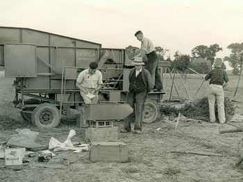 Beeld uit de jaren vijftig. Een dorsmachine voor bietenzaad, buiten op het land. Vier personen, maar wie zijn ze?  