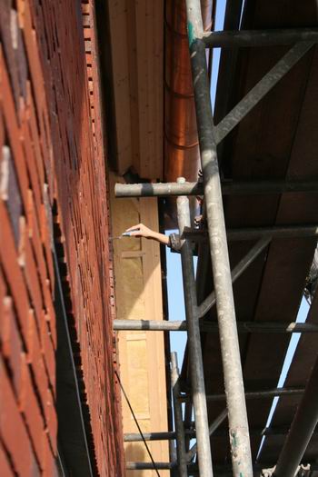 Marco Kooi zelf en een stagiaire bewerken de oostelijke topgevel. Karakteristiek, dat subtiele handgebaar....