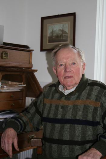 Schuiringa in zijn huidige woning aan de Hoofdstraat in Zuidhorn. Boven zijn hoofd een oude foto van de boerderij aan de Noorderweg.  