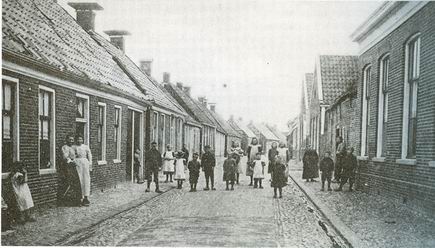 Foto van de Nieuwstraat, gezien vanaf de Langestraat, eerste kwart 20ste eeuw. Aan de rechterkant met de puntdaken de vroegere diakoniehuizen van de kerk, dicht op de straat. Zie Gisteren voor de Lens, bladzij 158)