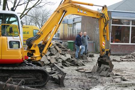 Grondwerker Jan Balkema onttegelt het terrein, vrijwilligers staan te popelen hun bijdrage te leveren 