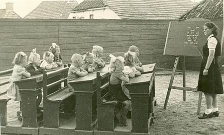 Kleuters in schoolbanken, juf Zaagman bij de lessenaar 