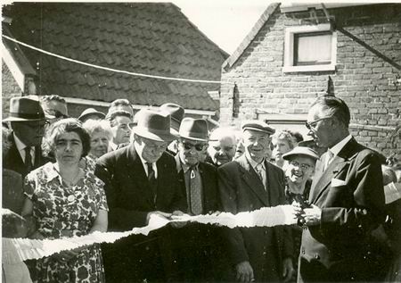 Een papieren feestslinger wordt doorgeknipt... Waar? Wanneer? Wie staan er op de foto? 