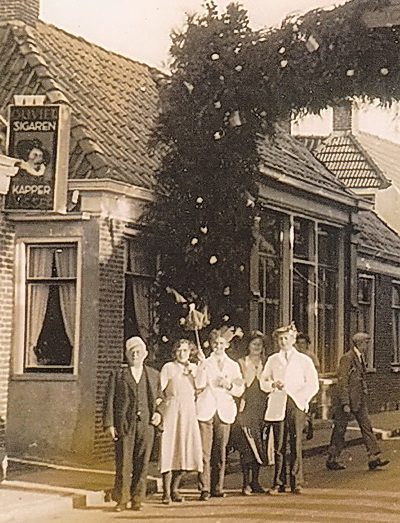 Een deel van de foto. Duidelijker? Links alleen het uithangbord met sigarenreclame van kapsalon Visser.  Volgens de familie Visser is de man links niét Jan Spoelma, maar opa Anne Visser! En die vrouw ernaast, Janna Dijkstra. Zus van Willy en Piet Helmus, nu wonend in Hoogkerk? Of mevr.Hoogstra-Dijkstra, Oldehove?