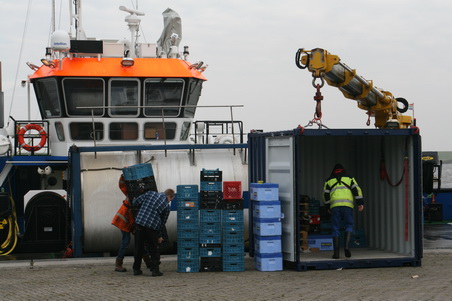 Kijk, de lege kratten e.d. zijn al bijna geheel uit de container, moeten wachten tot de trailer leeg is. Johannes Visser (met geel hesje) haalt de laatste spullen.