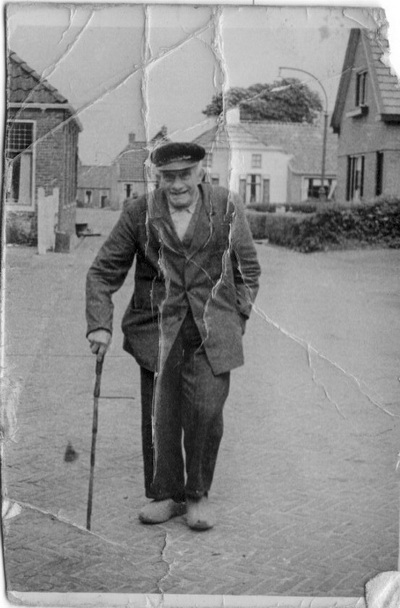 De oude Tjeerd van Hoogen, wandelend op de Achterweg. De wandelstok kwam uit Amerika, is nog steeds in het bezit van het nageslacht! Rechts, herkenbaar, het huis van de fam.Burgler. 