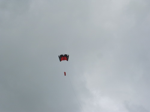 Hoog in de lucht een forse vlieger die ondanks het onstuimige weer stabiel op zijn plek hangt. Maar waar zijn de vliegeraars?