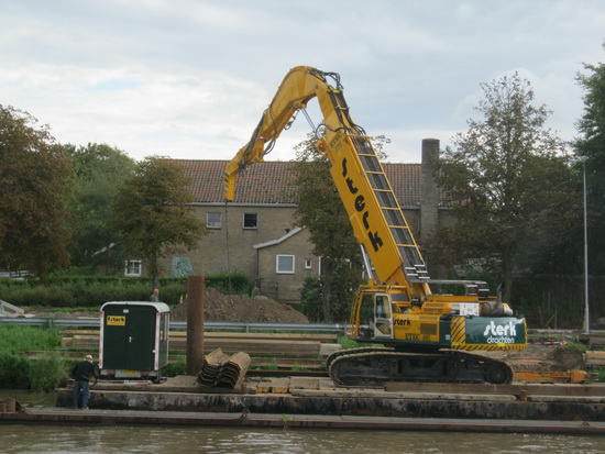 Gestaag gaat het werk aan de overkant verder. Hier wordt een lange ijzeren stut door de kraan opgetild en even later op zijn plaats gezet...