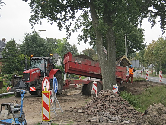 Een achteruit gereden kiepkar lost de gemalen-puin-inhoud op de plek waar een tijdelijke op/afrit komt, voor betonauto's.