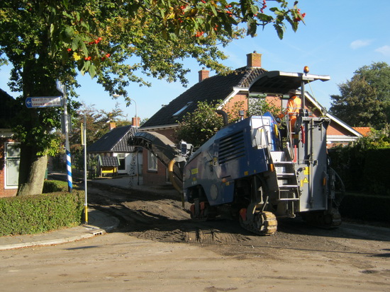 Het vreemdsoortige apparaat op rupsbanden neemt nu de plek in, voor aan de Noorderweg. Het laatste plaveisel moet worden weggewerkt. Schrapen, verkruimelen, op een vrachtwagen spuwen, afvoeren....