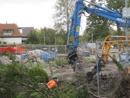 Te midden van het gevelde Kruisingagroen een blauwhelm met oranje jack (of pak?), beschermd door een blauwe GMB-arm...