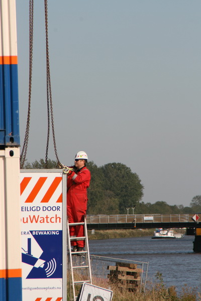 Aan de noordkant van het kanaal houden Gasunie-medewerkers zich bezig met onduidelijke werkzaamheden. Hier wordt een staander met plakkaat verplaatst met kraanhulp...