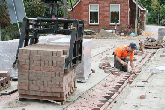 Links een keurige kubus straatstenen, die geheel of gedeeltelijk richting legmachine kan worden getild, door de grijper.