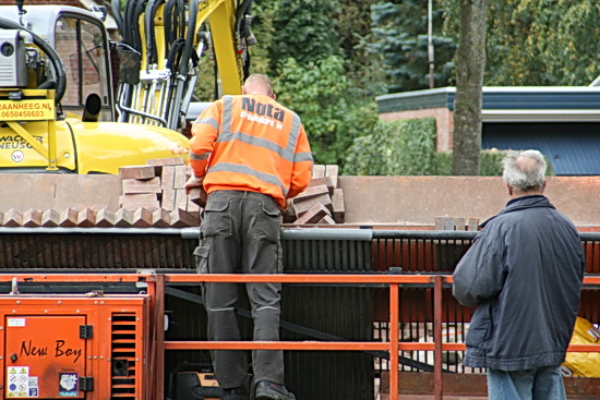 Zo ziet het eruit aan de andere kant van de brede machine. Een vakkundige legger, rechts een belangstellende buurtbewoner. Gewoonlijk zijn er twee stenenvleiers, maar de tweede wilde beslist niet op de foto....