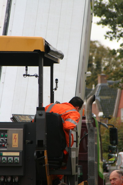 Voor de man op de asfalteermachine is het voortdurend opletten geblazen. Hij houdt het kettinkje langs de kant in het oog. Gaat de bestuurder van de vrachtwagen iets afwijken van de goede lijn, volgt er een druk op de claxon....