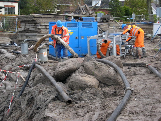 Twee blauwhelmen van GMB zijn met slangen en pompen bezig... Ja, in dit waterrijke jaargetijde moet je wel pompen. Een openluchtbad op deze plaats is onbruikbaar...