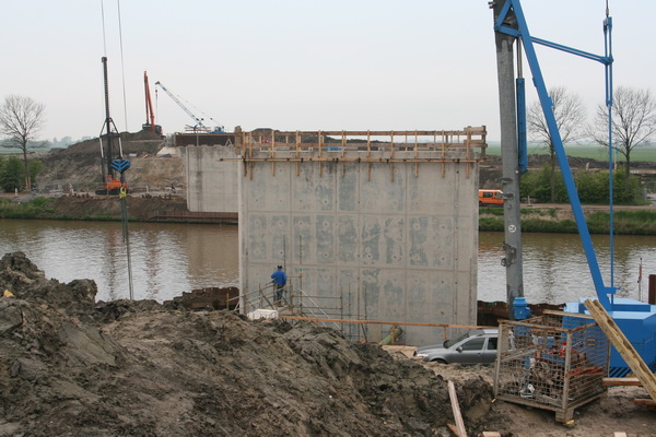 Foto vanaf de zuidkant van de bouwput van de nieuwe, vaste, hoge brug. Beide pijlers zijn al zonder bekisting. Aan de landhoofden wordt nog gewerkt.